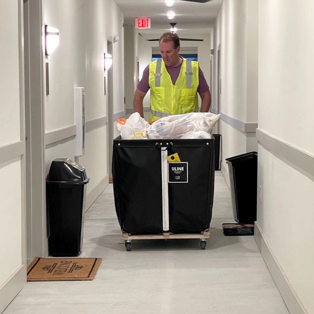 Valet trash collection in an apartment hallway with bagged trash on a cart